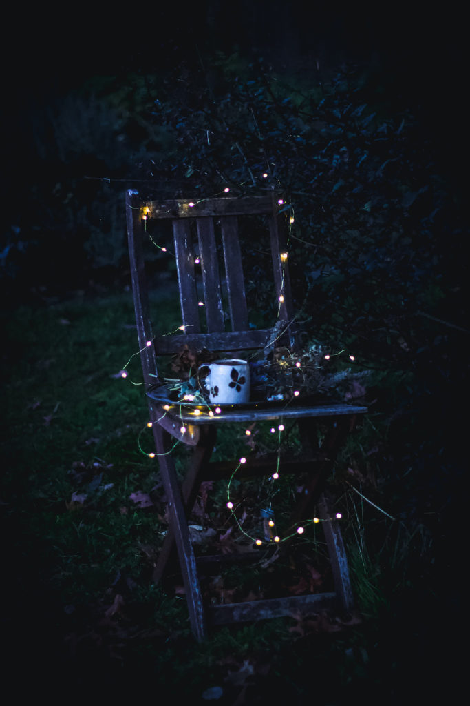 dried flowers and tea on tray on chair in dark outside with twinkle lights