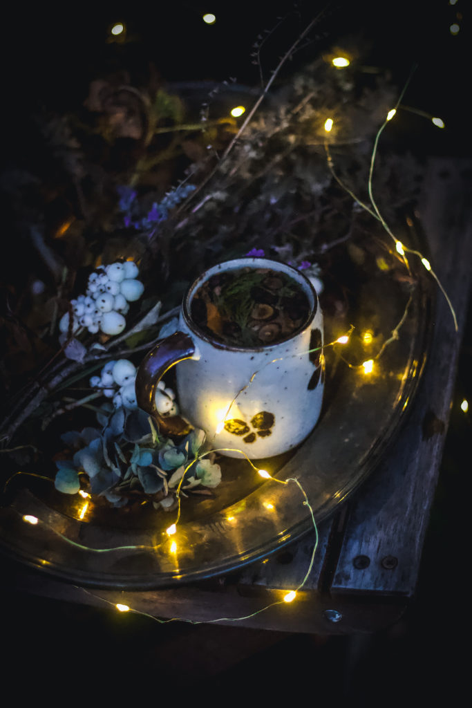 dried flowers and tea on tray on chair in dark outside with twinkle lights