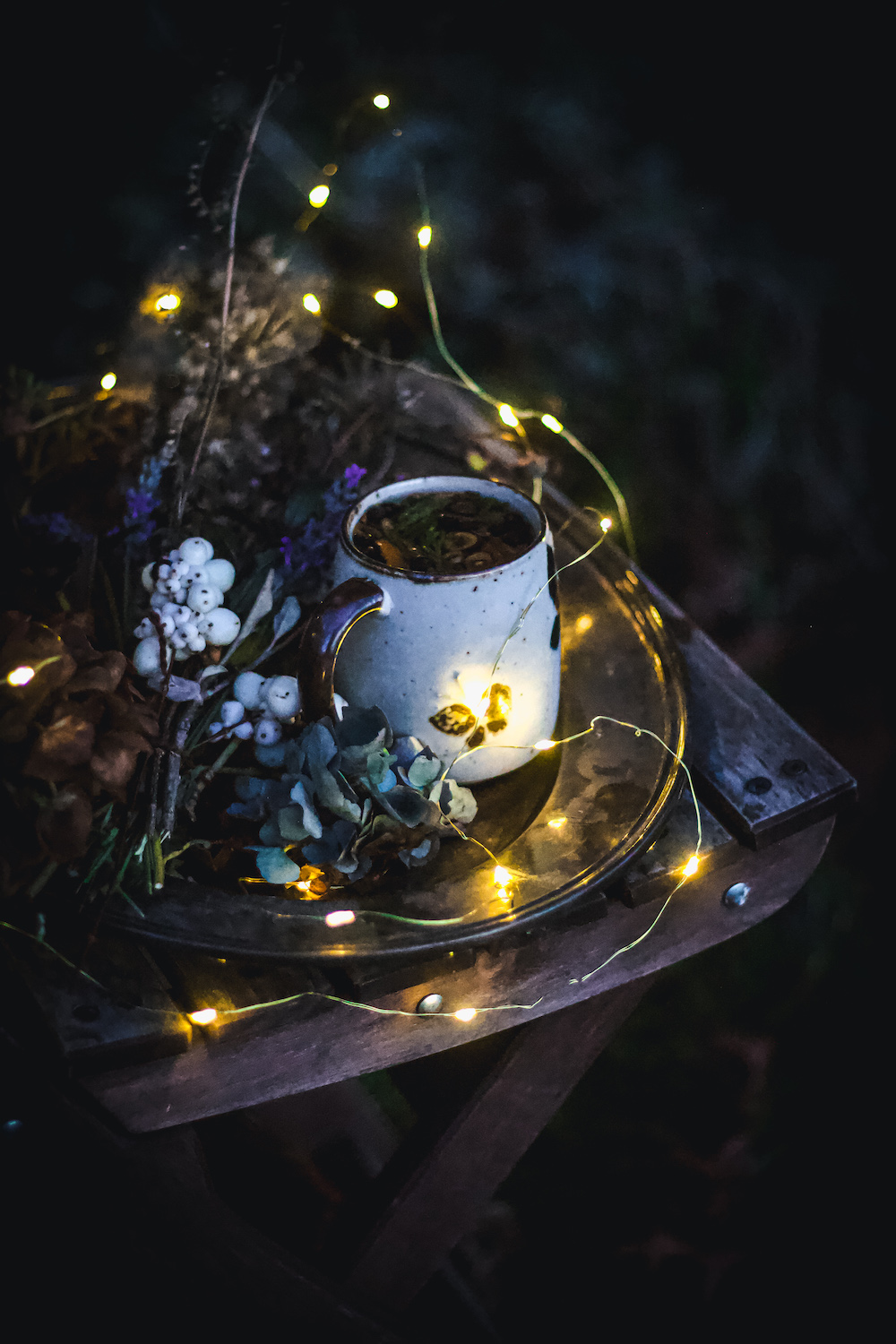 herbal tea in mug outside in dark with dried flowers and lights